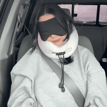 Woman resting in a car seat wearing CHOOKLY ergonomic memory foam travel neck pillow and sleep mask for comfortable travel rest
