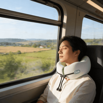 Traveler resting on a train seat wearing CHOOKLY ergonomic memory foam travel neck pillow for comfortable neck support during long journeys
